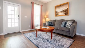 A living room with a sofa, a coffee table, a rug, a door, and a painting on the wall.