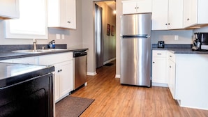 A modern kitchen with white cabinets, stainless steel appliances, and a wooden floor.
