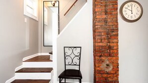 A staircase with wooden steps leading to a landing, a black metal chair, a brick wall, and a wall-mounted clock.