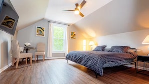 A bedroom with a bed, a desk, a chair, a ceiling fan, and a window with curtains.