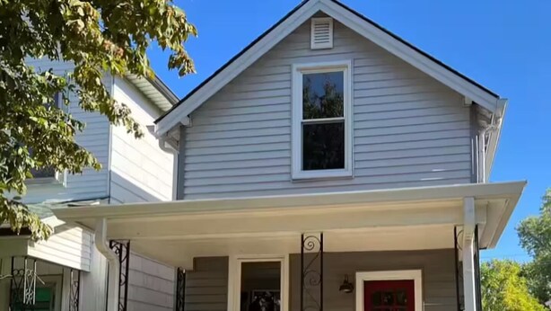 A two-story house with a covered porch, a red door, and a small front yard.