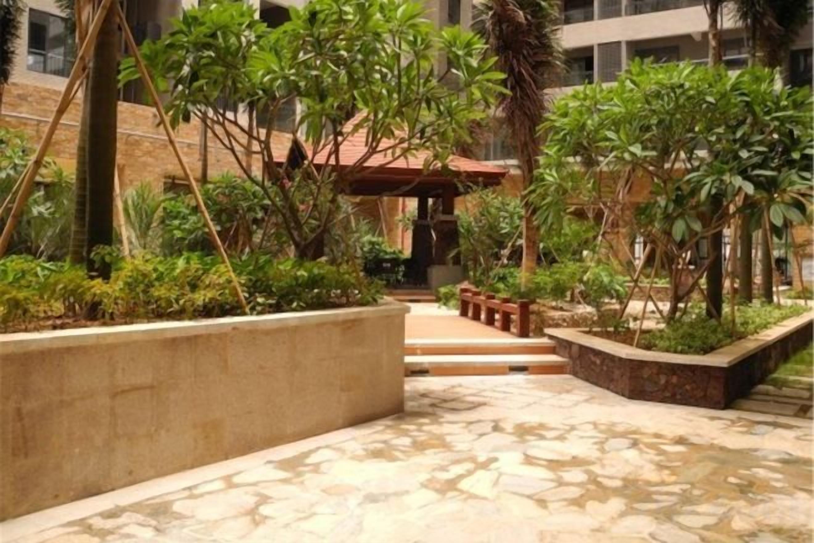 Une cour avec un sol en pierre, des jardinières remplies de verdure et un bâtiment en arrière-plan.