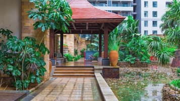 A covered outdoor area with steps leading to a building entrance, surrounded by greenery and a water feature.