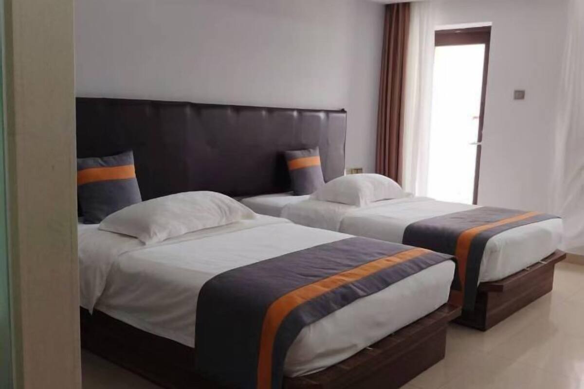 Ein Hotelzimmer mit zwei Betten, jeweils mit Kopfteil, weißer Bettwäsche und orange-blau gestreiften Tagesdecken.