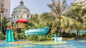 Zona de piscina con un barco azul grande, palmeras y un edificio con cúpula al fondo.