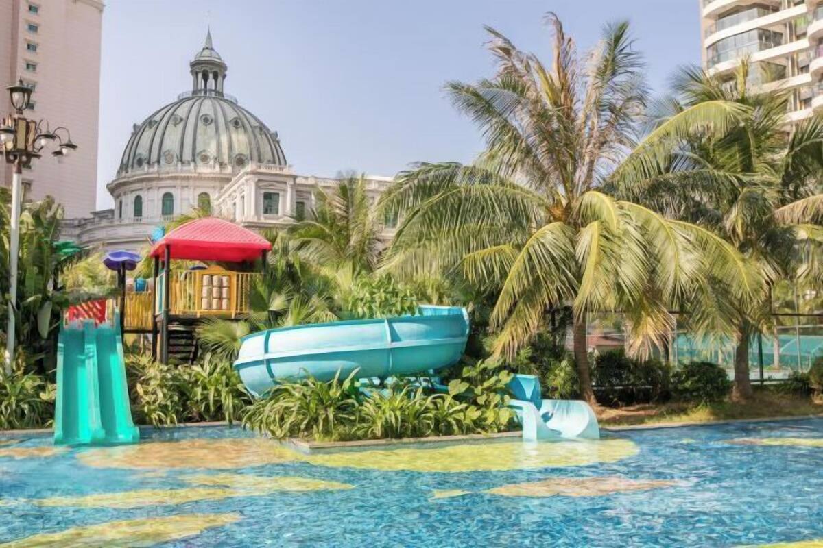 Ein Poolbereich mit einem großen, blauen Boot, Palmen und einem Gebäude mit einer Kuppel im Hintergrund.