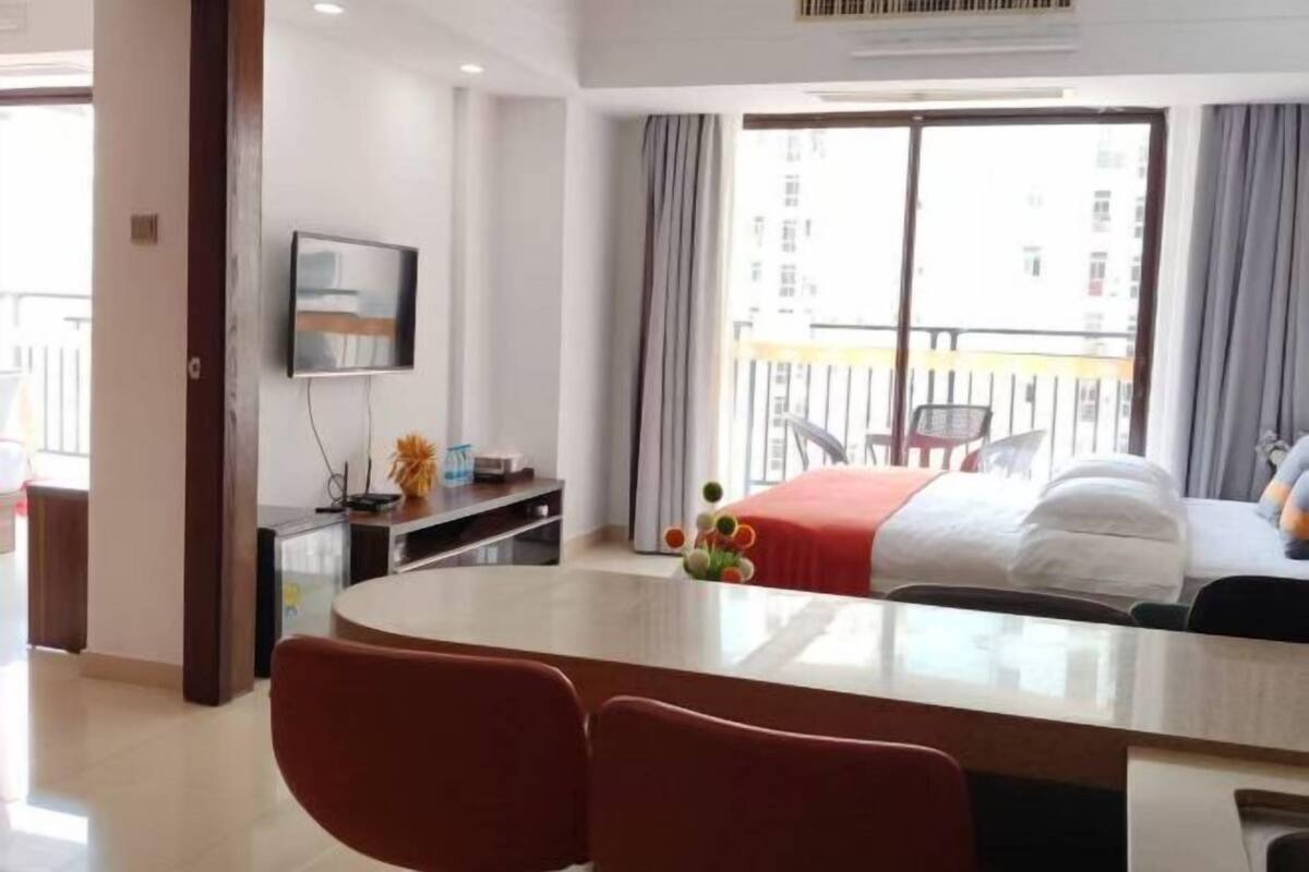 Ein Hotelzimmer mit Bett, Schreibtisch, Sessel, Fernseher und einem Balkon mit Vorhängen.