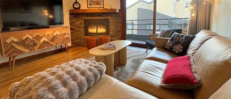 A living room with a flat-screen TV, a fireplace, a sofa, and a large window.