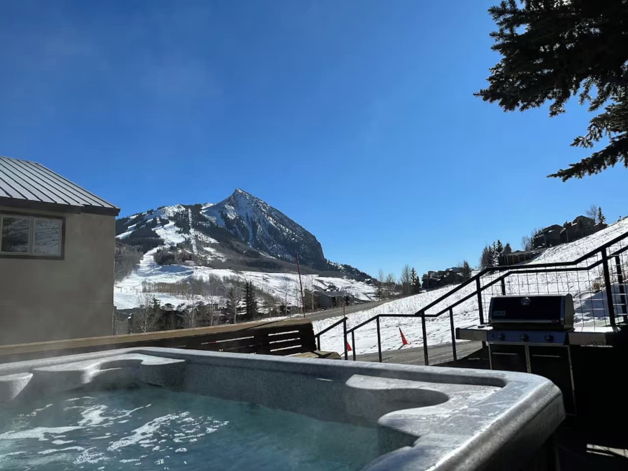 A hot tub with a mountain view, a barbecue grill, and a wooden deck.
