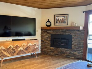 A living room with a flat-screen TV, a stone fireplace, and a wooden entertainment unit. - 5 Min. Free Shuttle to Resort•Mountain Views•Hot Tub•Sauna•Private Garage (Crested Butte)