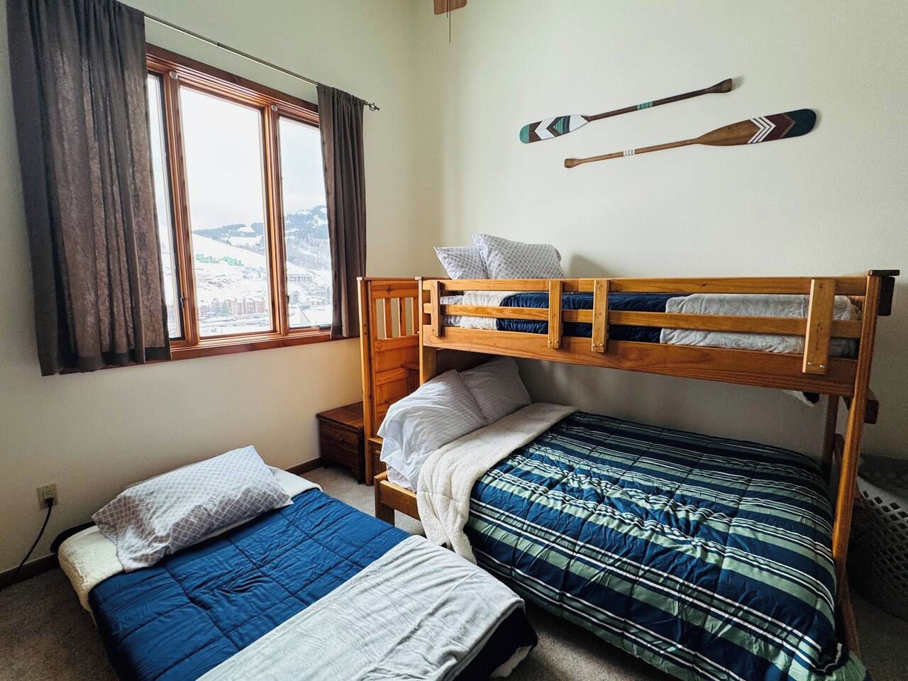 Ein Zimmer mit zwei Etagenbetten, einem fenster mit Vorhängen und einem an der Wand befestigten Surfbrett.