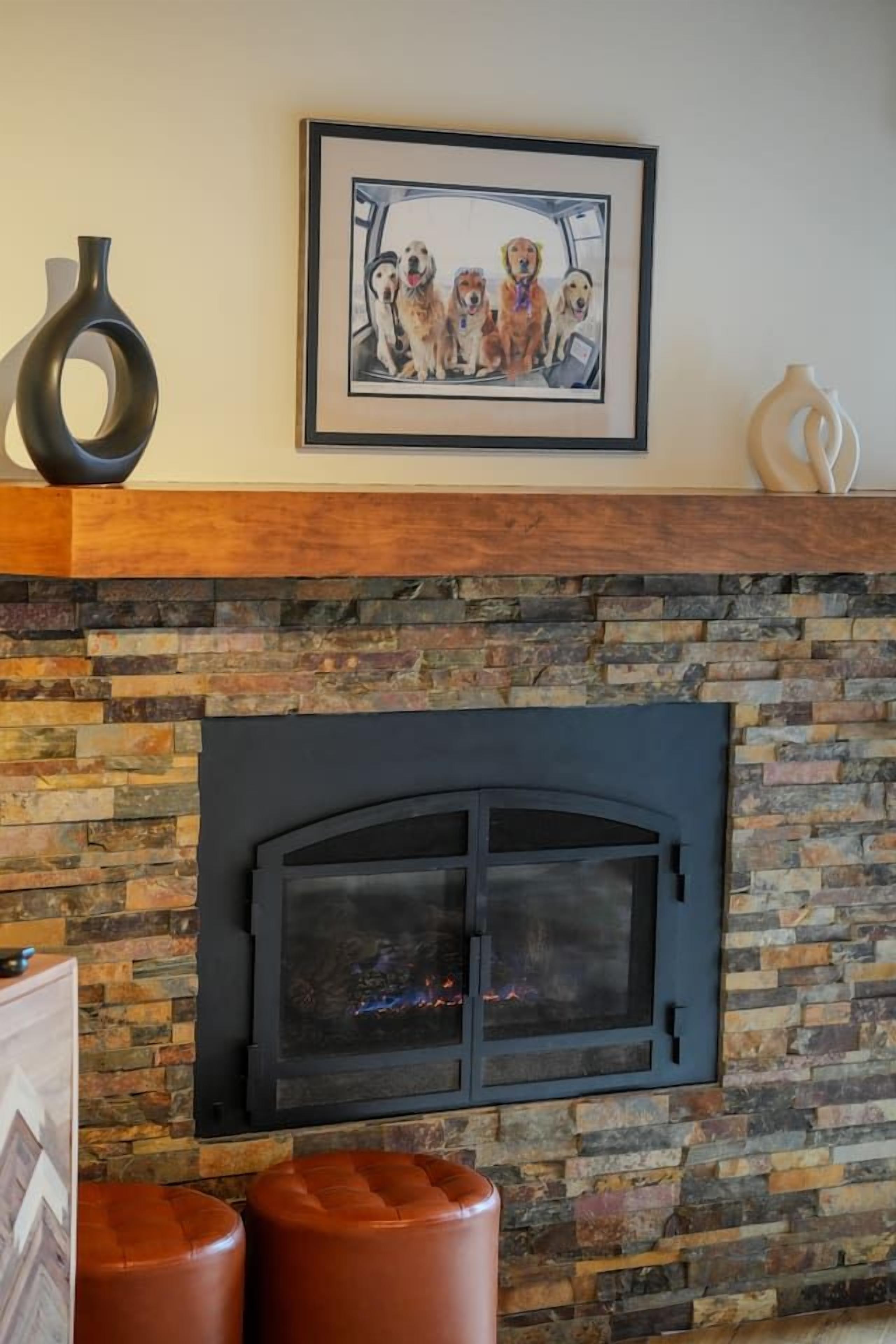 A fireplace with a stone surround, a framed picture above it, and two leather ottomans.