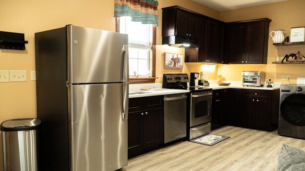 A modern kitchen with stainless steel appliances, dark wooden cabinets, and a tiled backsplash. - Cozy 1-bedroom apartment in quaint Creedmoor with AC, WiFi &laundry (Creedmoor)