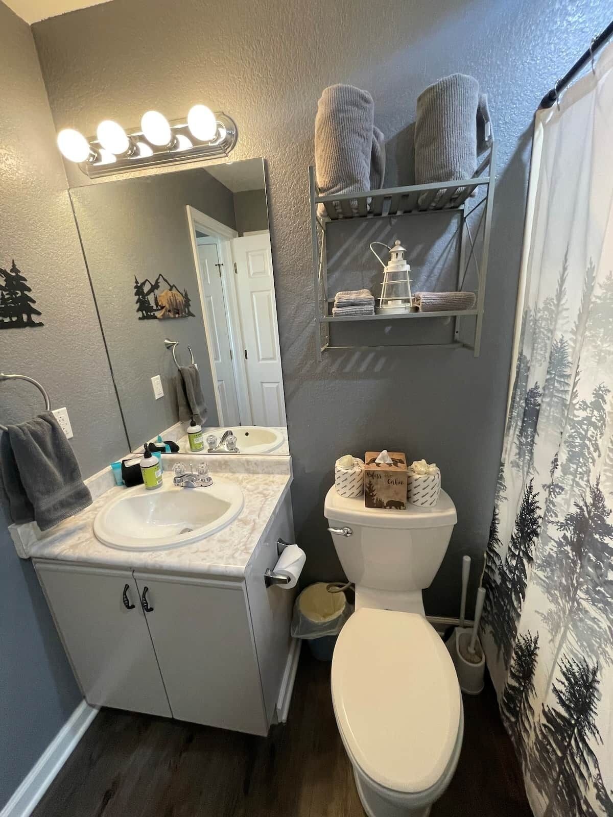 A bathroom with a white sink, mirror, and toilet. There are towels and toiletries on the shelves.