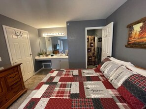 Un dormitorio con cama, cómoda, tocador con espejo y puerta que da a otra habitación.
