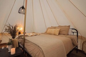 Habitación tipo tienda de campaña con una cama, una lámpara colgante y una pequeña mesa con velas y una planta.