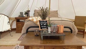 Et teltindrettet rum med seng, et træbord med skilt, lampe og en lille plante.