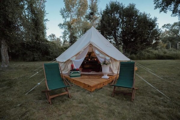 Una carpa con una plataforma de madera y dos sillas verdes al frente.