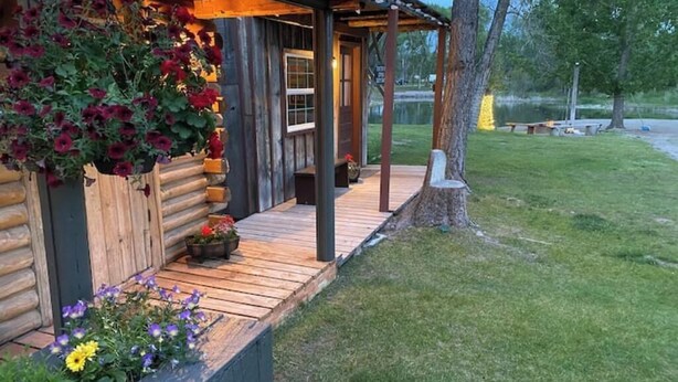 En træhytte med en træterrasse, blomsterkasser og udsigt til en sø.