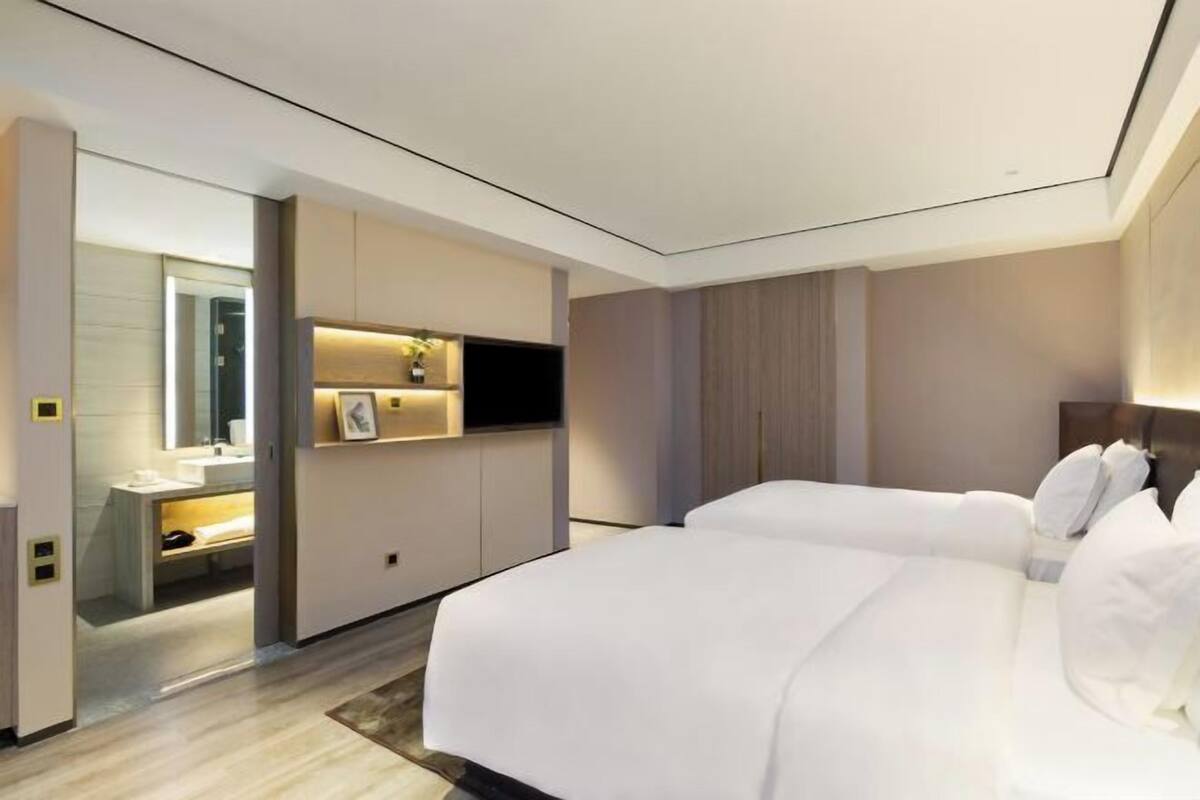 Une chambre d’hôtel moderne dotée d’un grand lit, d’un téléviseur intégré, d’une coiffeuse avec miroir et d’un petit coin salon.