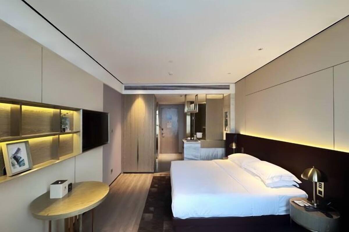 Une chambre d’hôtel moderne équipée d’un lit, d’une table de chevet, d’une lampe, d’une télévision et d’un petit bureau avec une chaise.