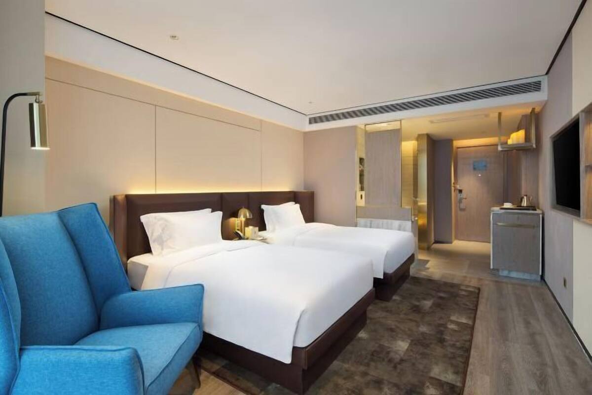 Une chambre d’hôtel avec un grand lit, un fauteuil bleu, une télévision et un petit bureau.