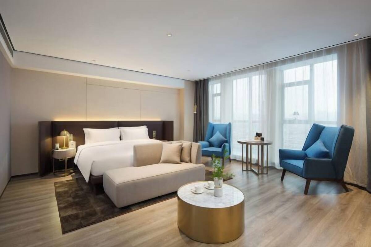 Une chambre d’hôtel moderne comprenant un lit, un canapé, deux fauteuils, une table basse et une petite table avec une lampe.