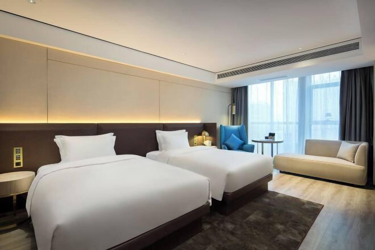 Une chambre d’hôtel avec deux lits, un canapé, une petite table et une fenêtre avec des rideaux.