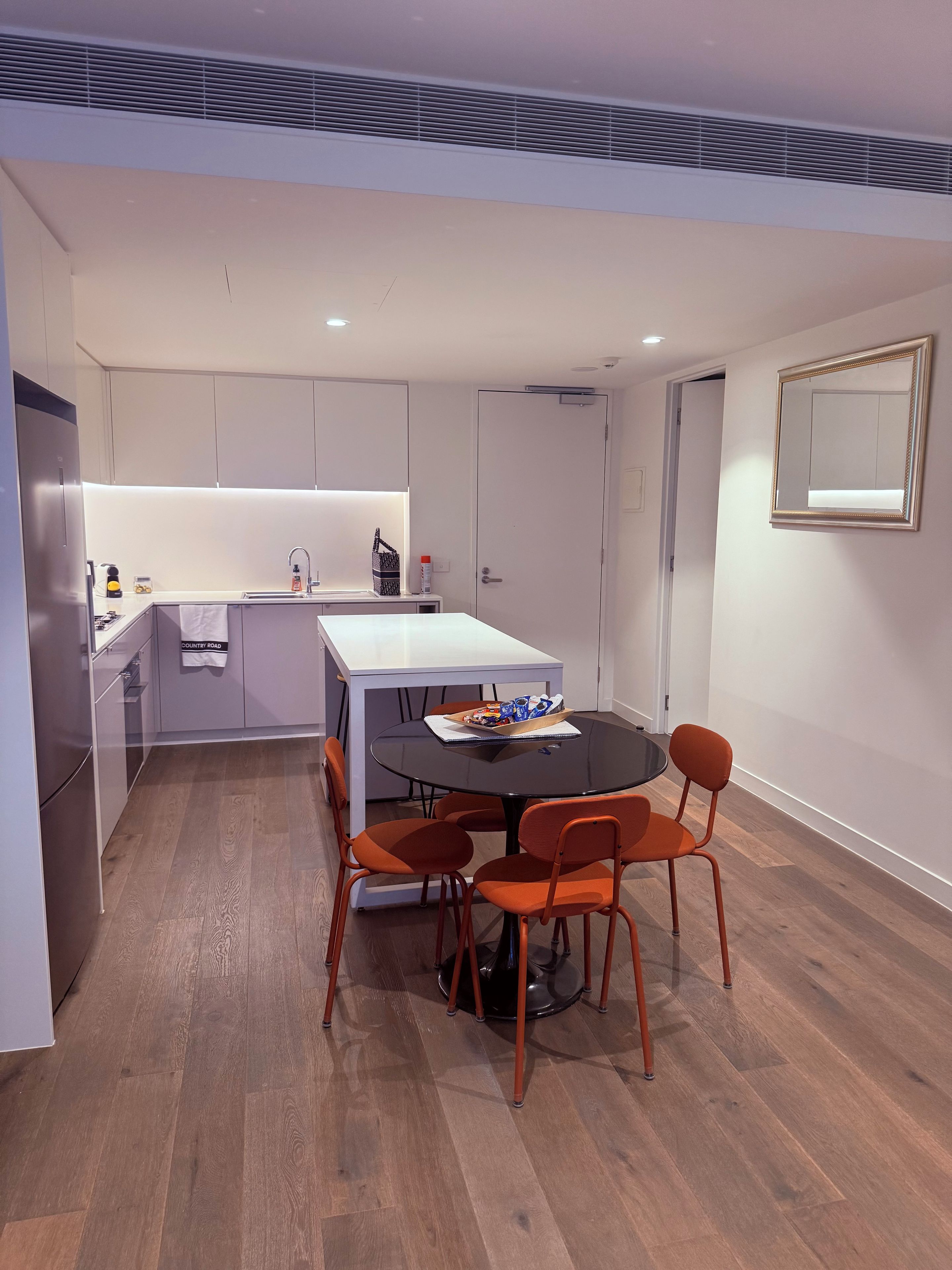 A modern kitchen with a dining area, featuring a round table with chairs, a built-in oven, and a white countertop.
