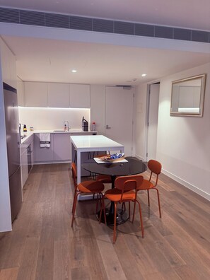 A modern kitchen with a dining area, featuring a round table with chairs, a built-in oven, and a white countertop. - Enjoy the local vibe & city surroundings + parking. Modern & family friendly. (Collingwood)