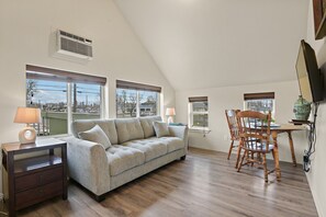A cozy living room with a sofa, a wooden dining table with chairs, and large windows offering a view of the outside. - Maple Manor City View (Spokane)
