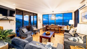 Un salón amplio con un gran ventanal que ofrece vistas panorámicas, un comedor con mobiliario de madera y una zona de estar acogedora.