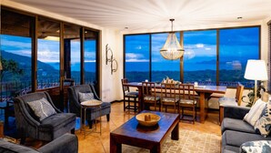 Un salón espacioso con una amplia mesa de comedor, asientos cómodos y ventanas grandes que ofrecen vistas panorámicas.