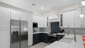 A modern kitchen with white cabinets, stainless steel appliances, a built-in oven, and a marble countertop.
