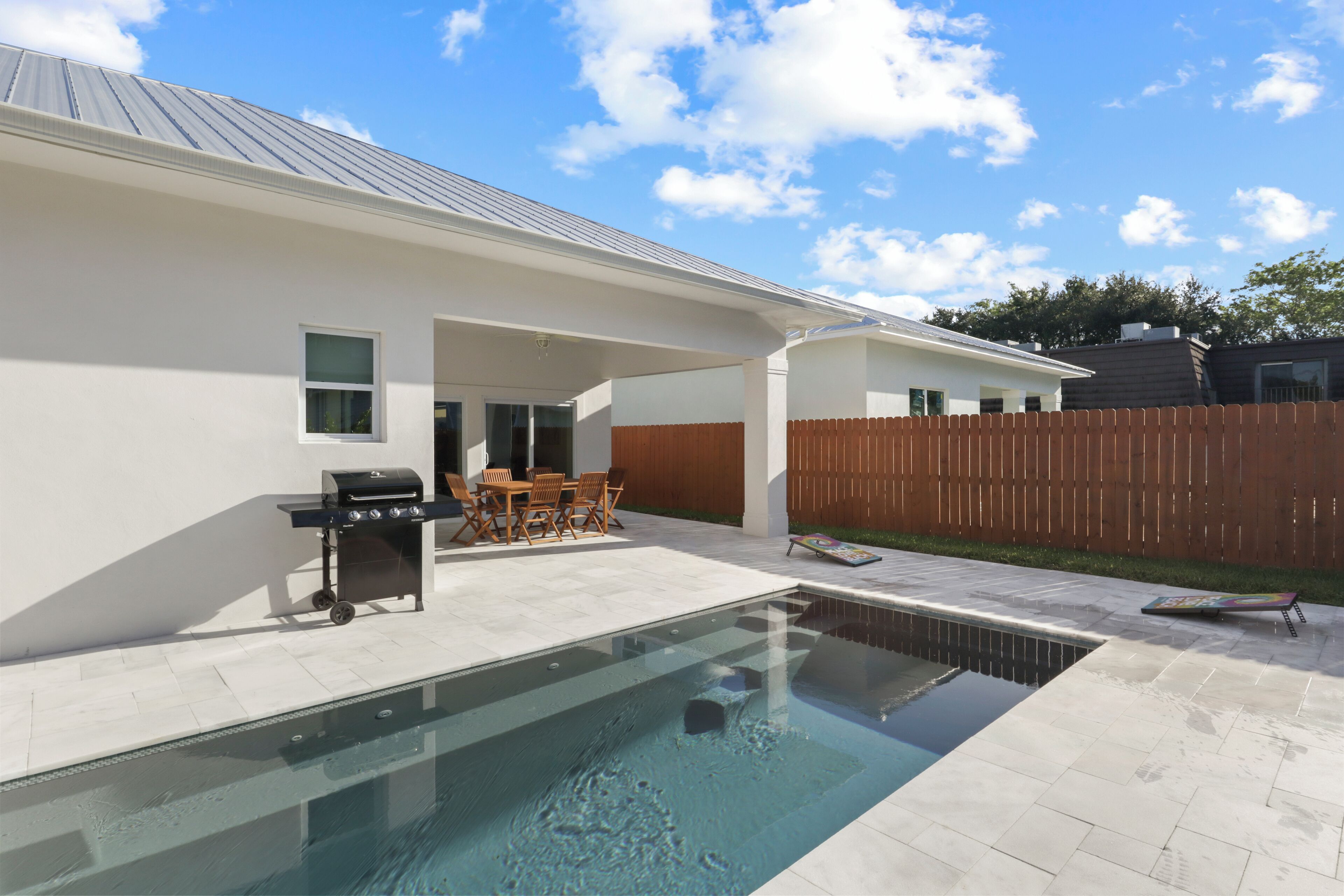 A swimming pool with a patio area, a barbecue grill, and a wooden fence in the background.