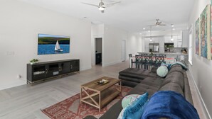A modern living room with a large flat-screen TV, a dark-colored sofa, a wooden coffee table, and a red patterned rug.