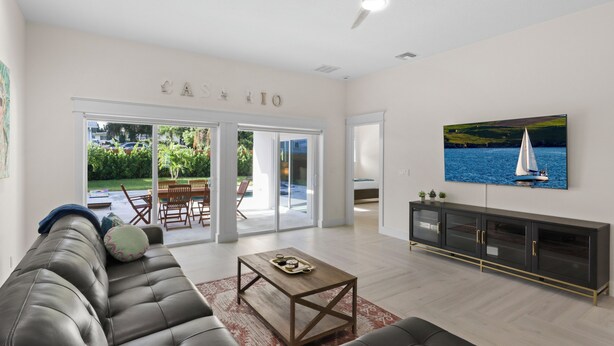 A spacious living room with a leather sofa, a wooden coffee table, and a large TV on the wall.