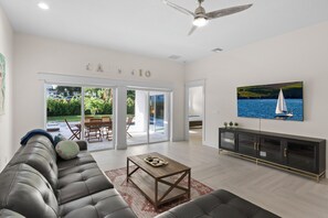 A spacious living room with a leather sofa, a wooden coffee table, and a large TV on the wall.