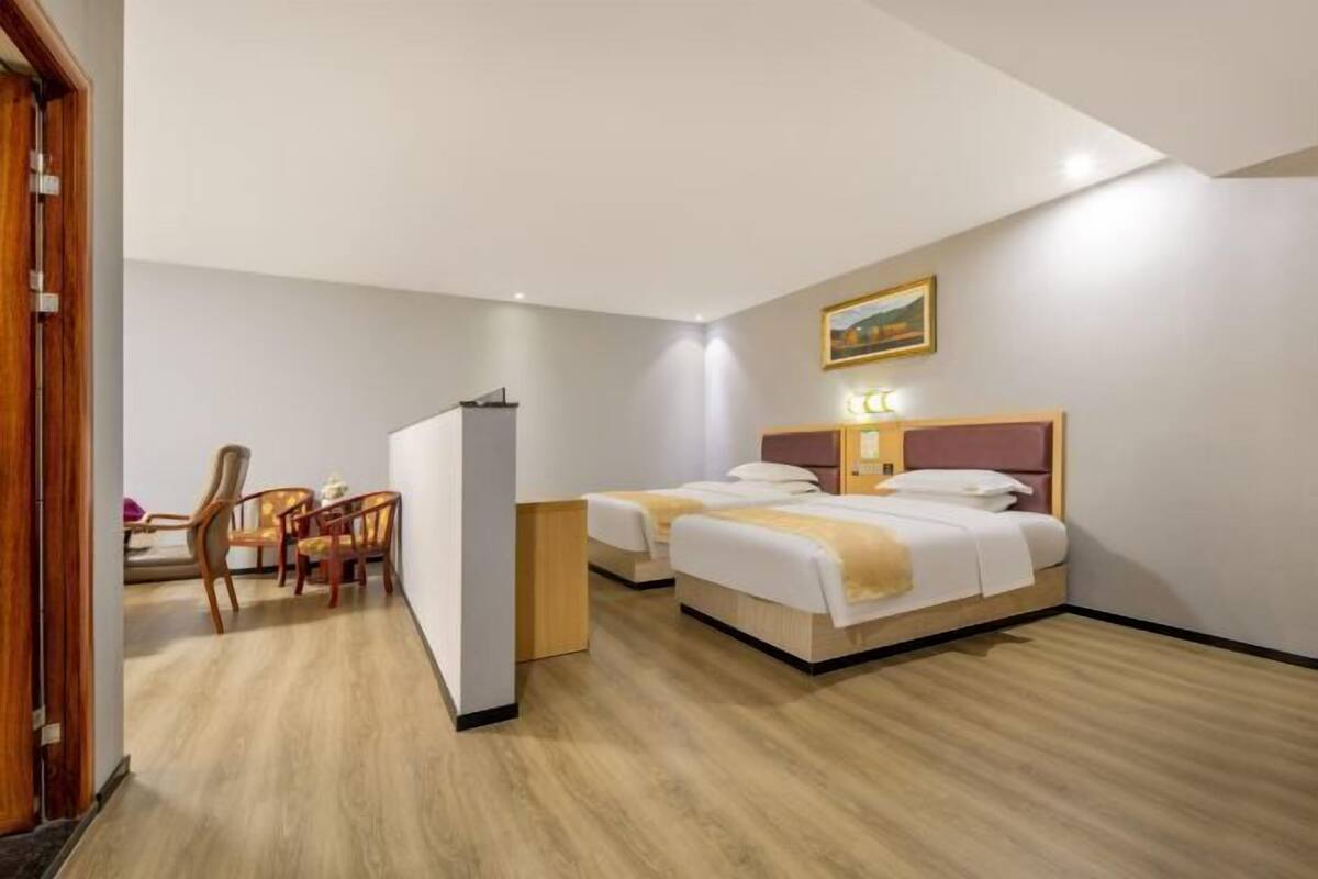 Een hotelkamer met twee bedden, een bureau met stoelen, een koelkast en een schilderij aan de muur.