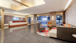 Un moderno vestíbulo de hotel con mostrador de recepción, zona de estar y amplios ventanales con vistas a la ciudad.