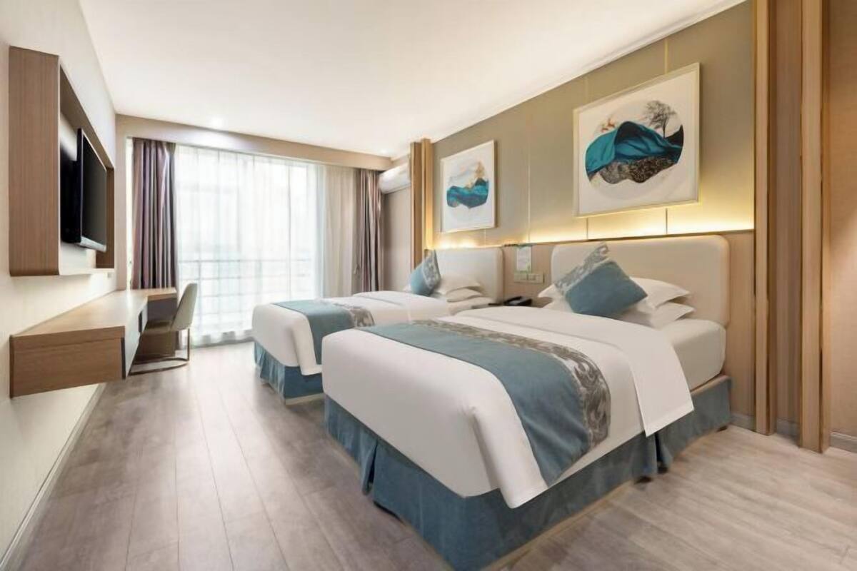 Een hotelkamer met twee bedden, een bureau, een televisie en kunstwerken aan de muur.
