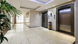 Un moderno vestíbulo de hotel con suelo de mármol, dos ascensores y una gran planta en maceta.