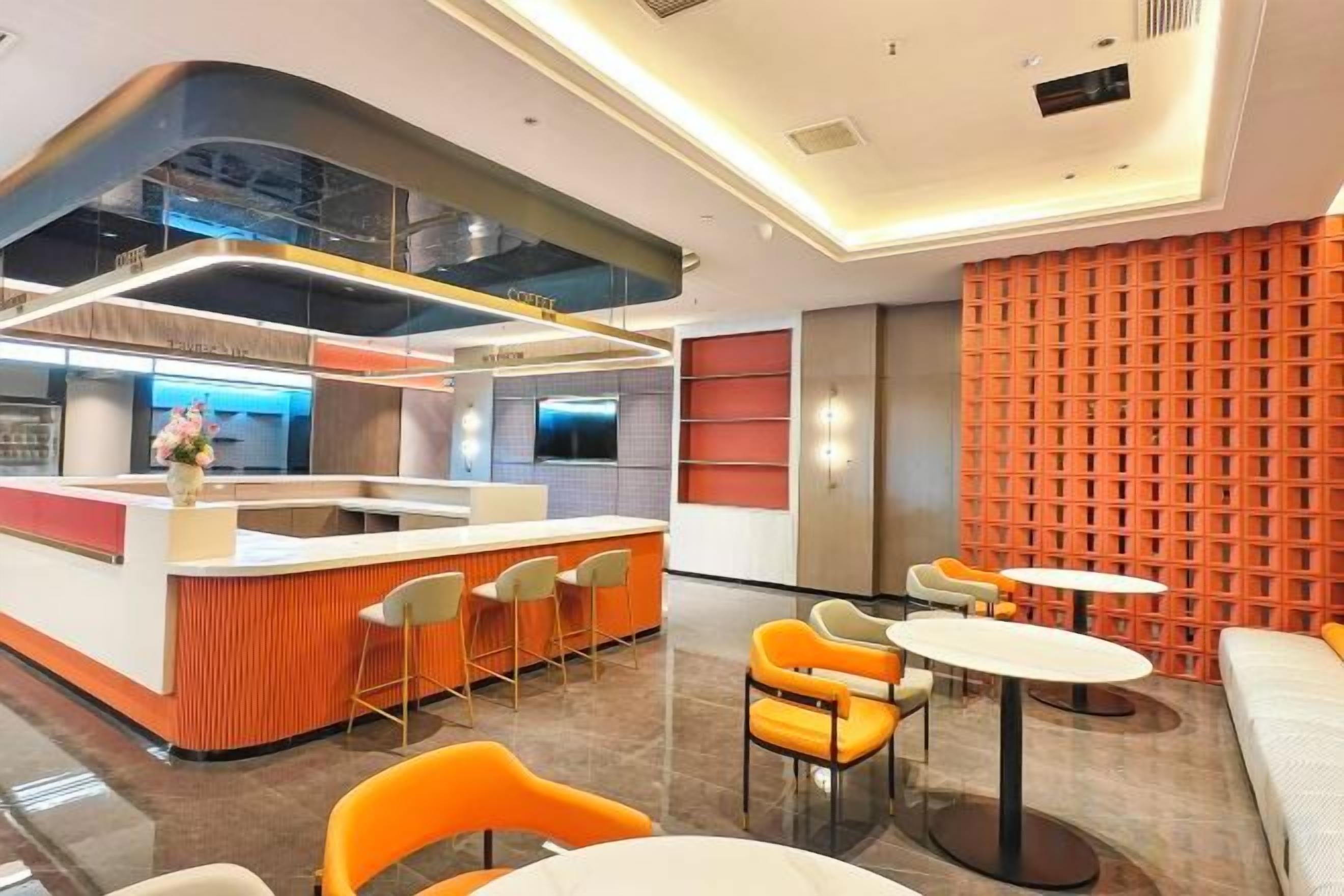 A modern hotel lobby with a central bar area, seating arrangements, and a patterned wall.
