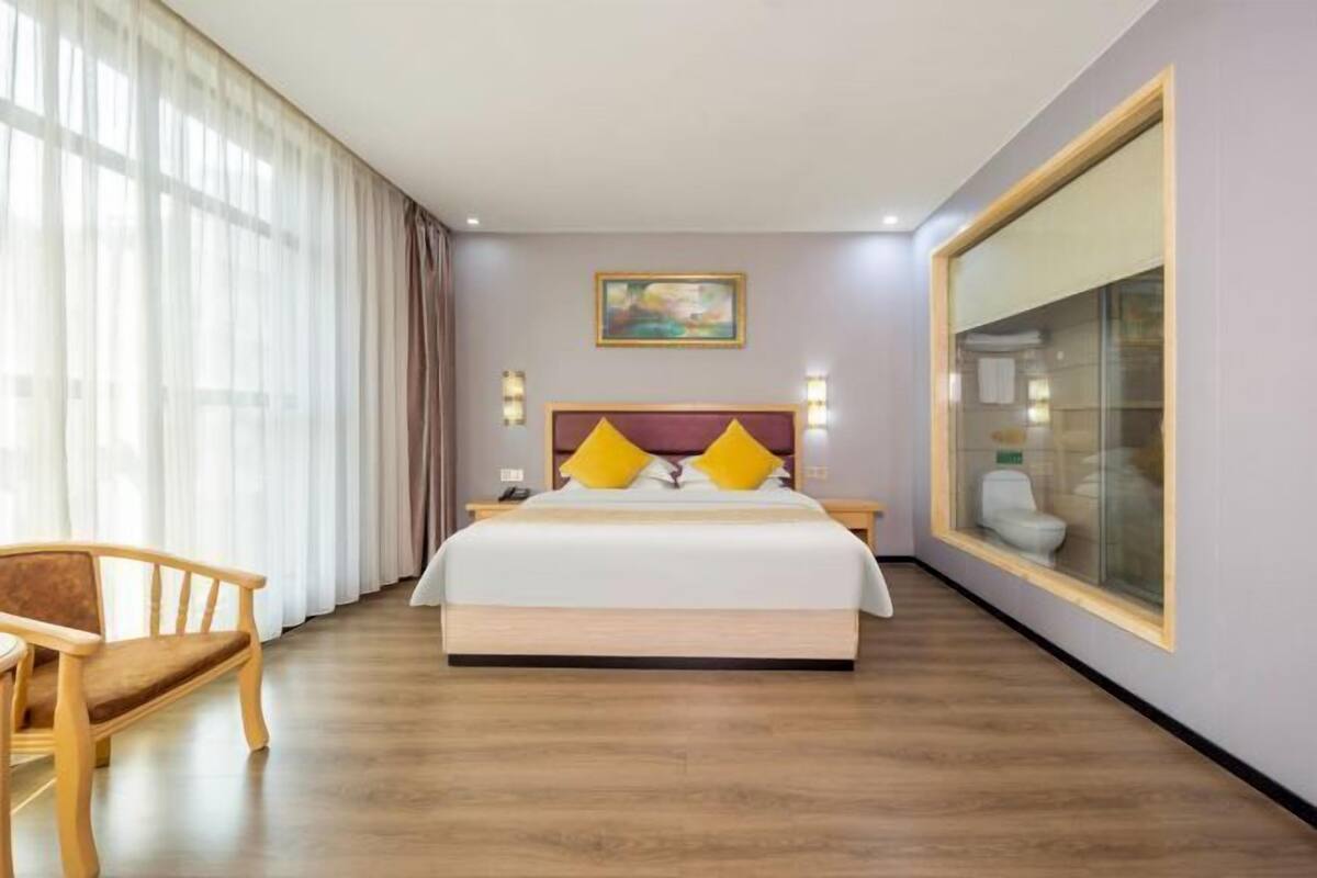Een hotelkamer met een bed, een houten stoel, een schilderij aan de muur en een groot raam.