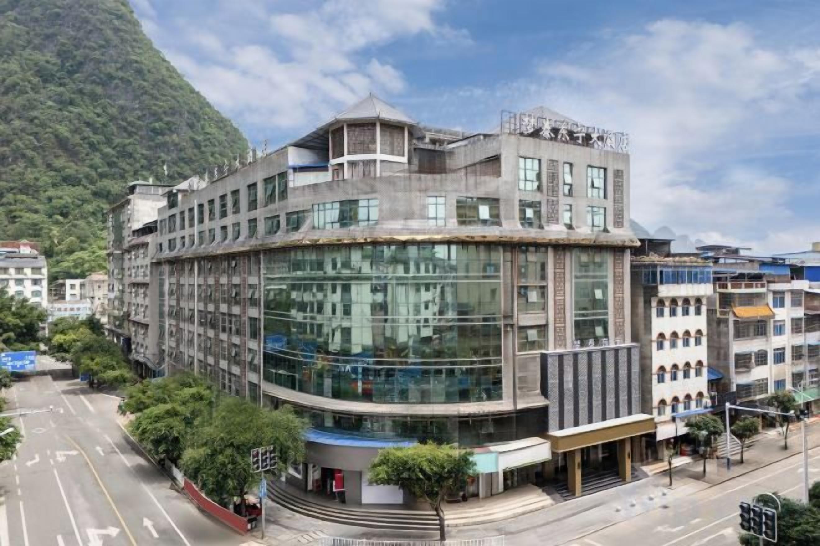 A multi-story building with a curved glass facade, located near a road with a mountain backdrop.