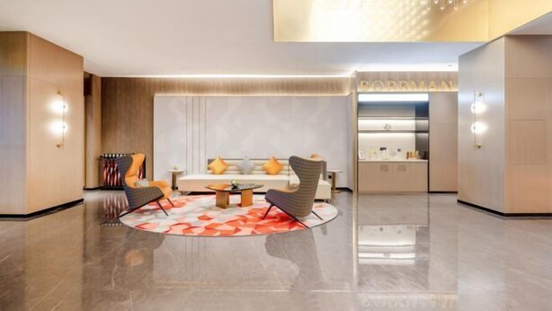 Un moderno vestíbulo de hotel con una zona de estar central, un mostrador de recepción y una cocina.