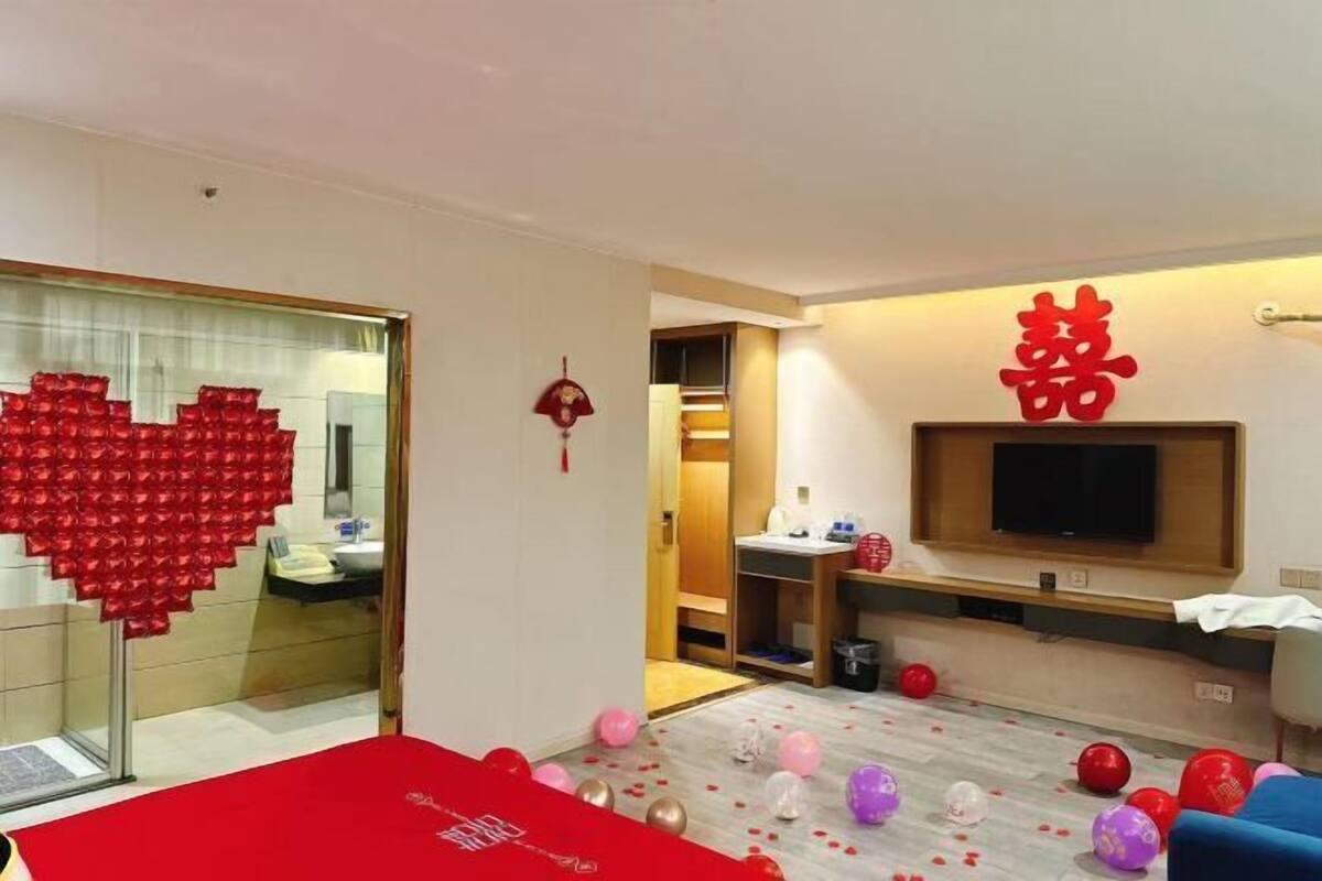Een moderne woonkamer met een hartvormige decoratie op de glazen deur, een wandtelevisie en verspreide ballonnen op de vloer.