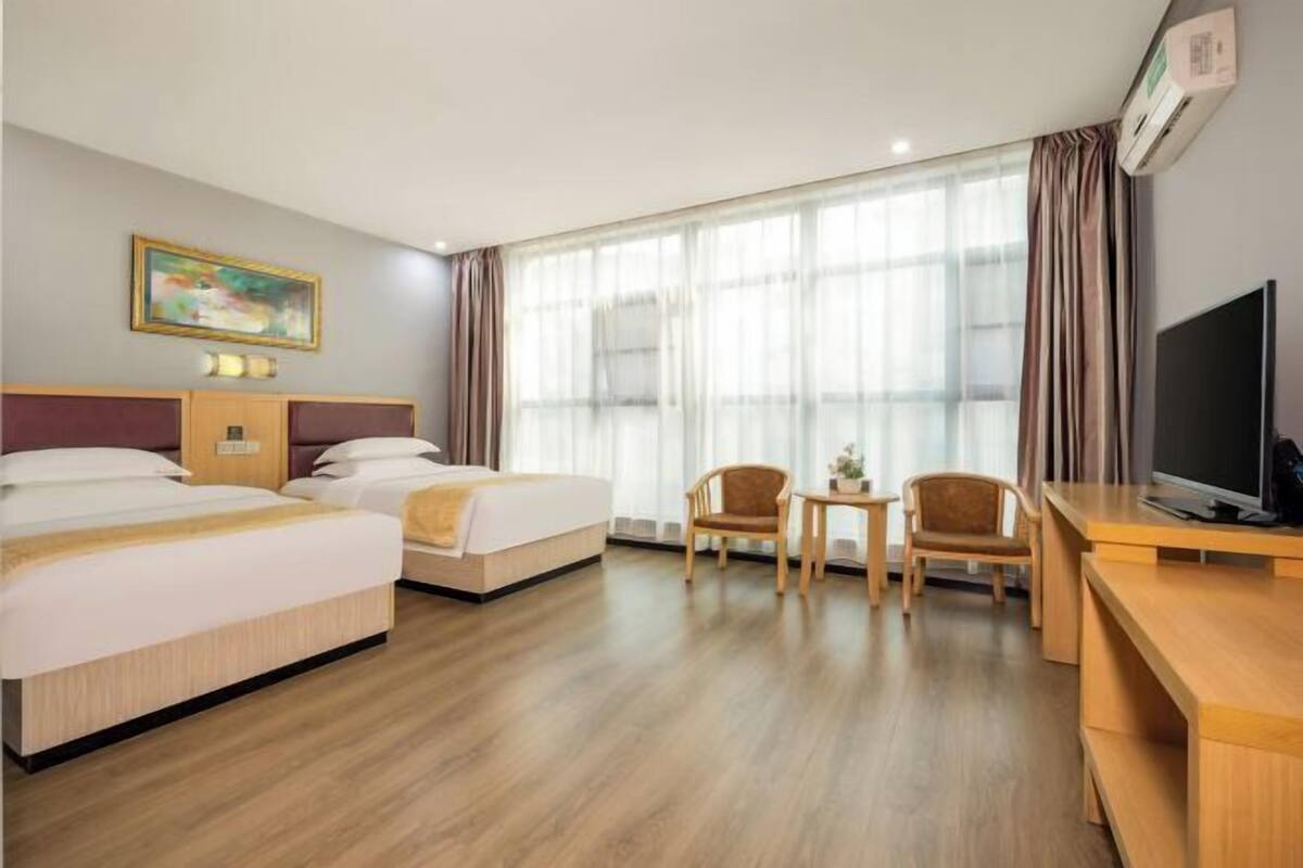 Een hotelkamer met twee bedden, een bureau, een stoel, een televisie en een groot raam met gordijnen.