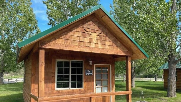 Une cabane en bois avec un toit vert, une véranda et une enseigne sur laquelle on peut lire : « The Ranch House ».
