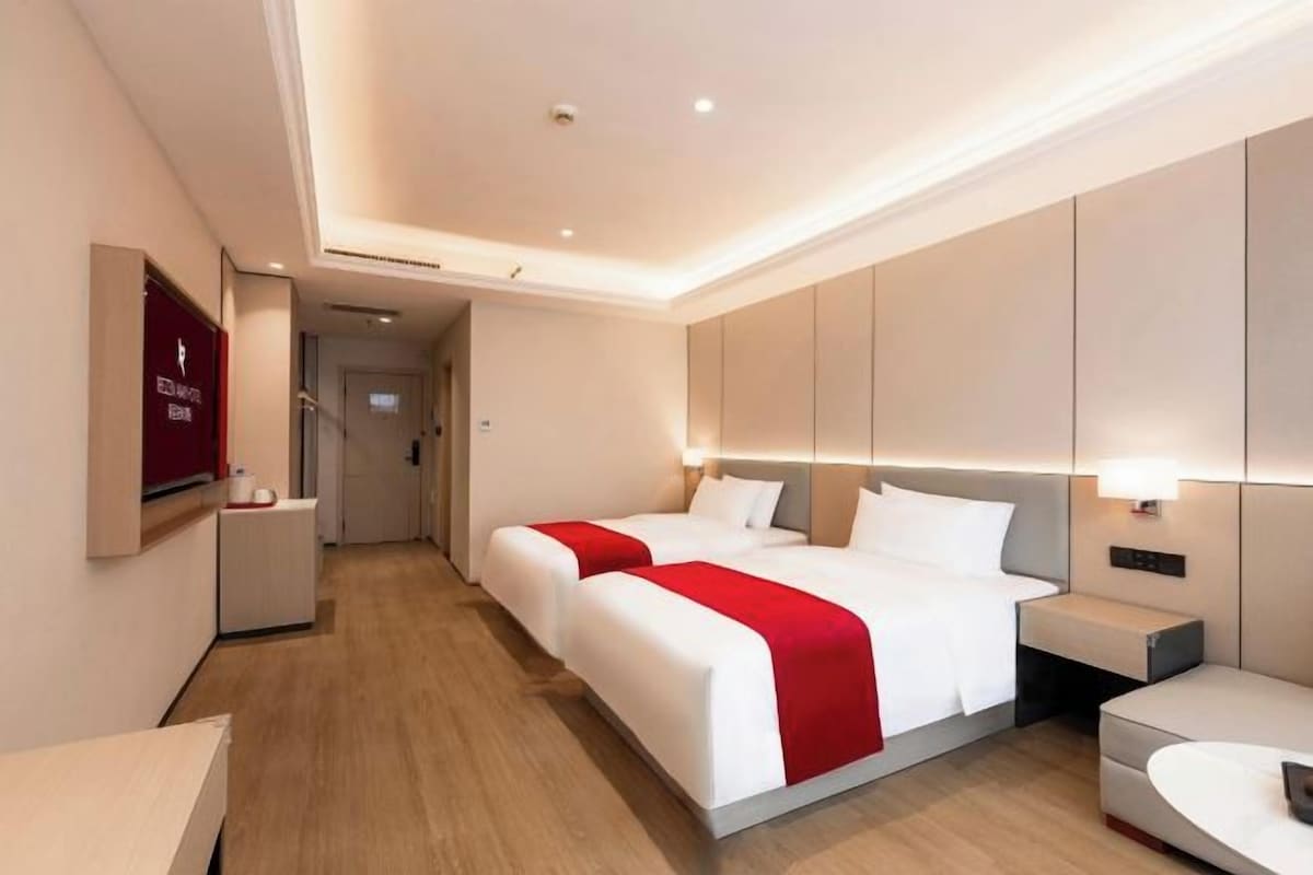 A hotel room with two beds, a bedside table, a desk, and a TV.